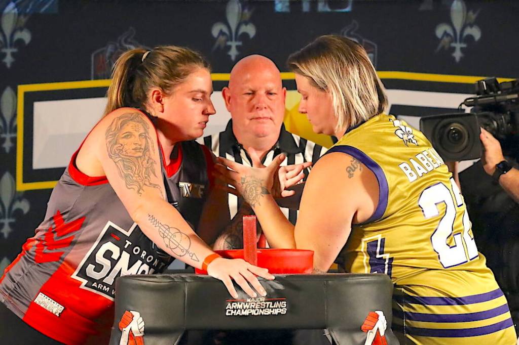 Team arm wrestlers Danika Lavigne, left, and Tiffany Barbeau with ref Craig Michell during a pre-season showcase for Team Arm Wrestling Federation (TAWF) in Toronto in October 2025. (Contributed/TAWF photo)
